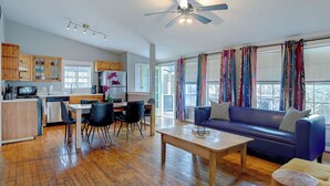 Una cocina moderna con armarios de madera, una zona de comedor con mesa y sillas, un sofá azul y un ventilador de techo.
