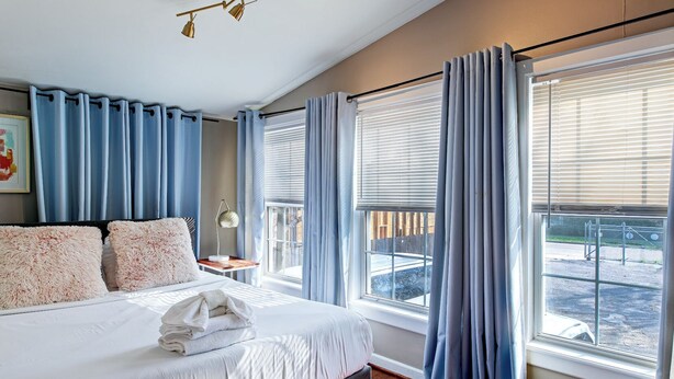 Un dormitorio con cama, mesita de noche, lámpara y cortinas.