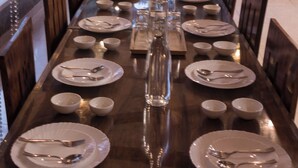 A long dining table set with plates, cutlery, and glasses, surrounded by chairs, with a view of greenery outside. - Moonstone Meadows Suite By Alaya Stays (Mawal)