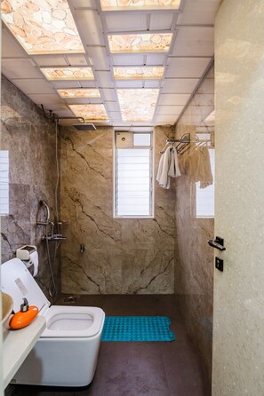 A bathroom with a toilet, shower, and a window. - Moonstone Meadows Suite By Alaya Stays (Mawal)