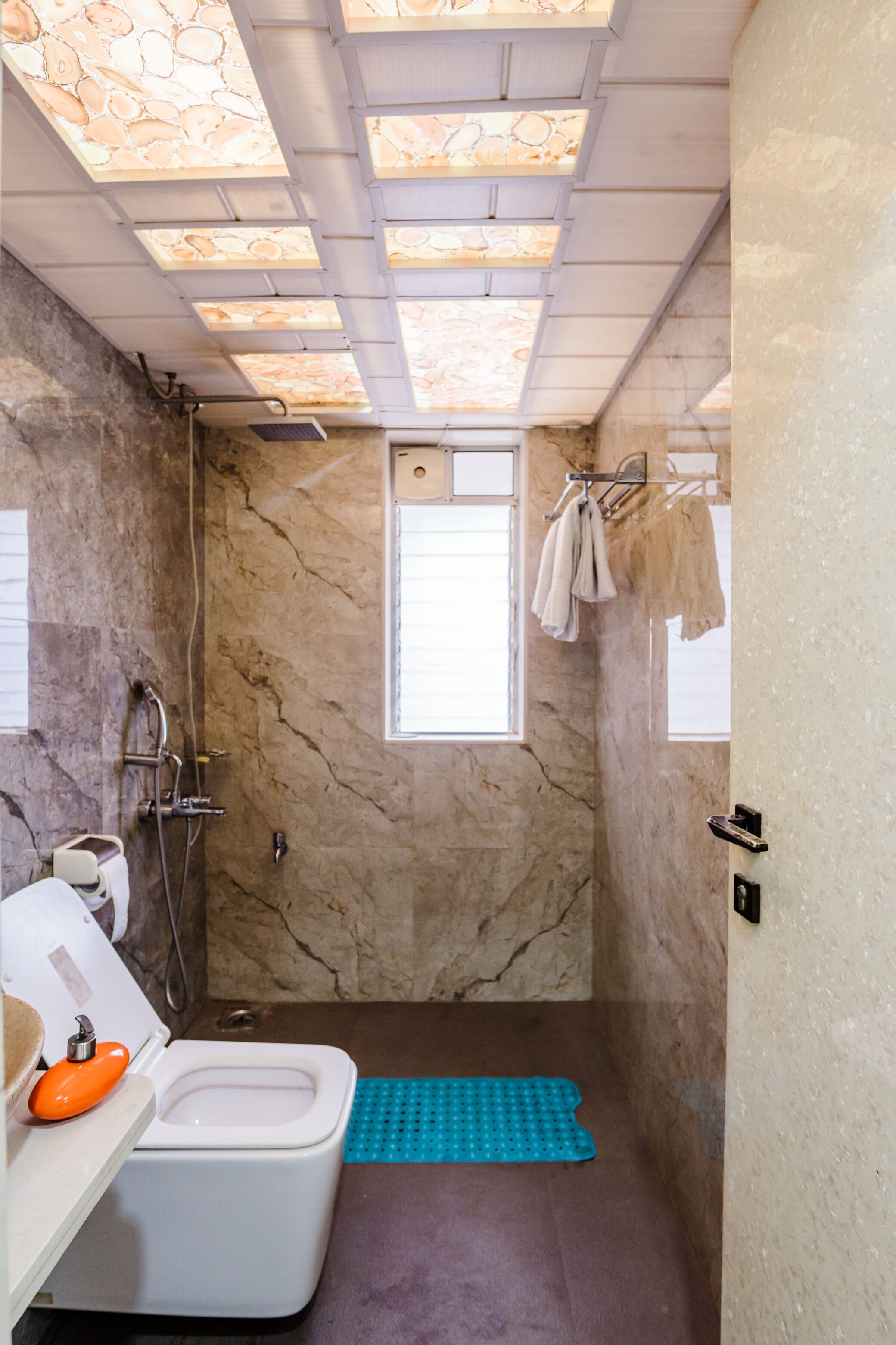 Un baño con pared de mármol, ducha, inodoro y ventana.