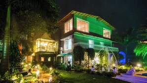 A two-story house with a balcony, surrounded by lush greenery and illuminated by artificial lighting. - Moonstone Meadows Suite By Alaya Stays (Mawal)