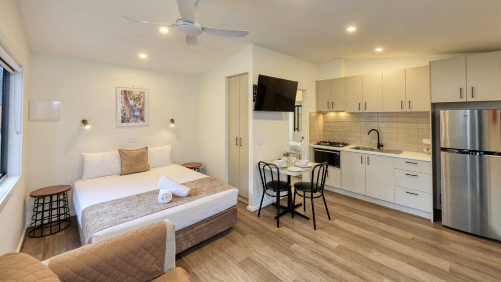 A modern hotel room with a bed, bedside table, and a small dining area with chairs.