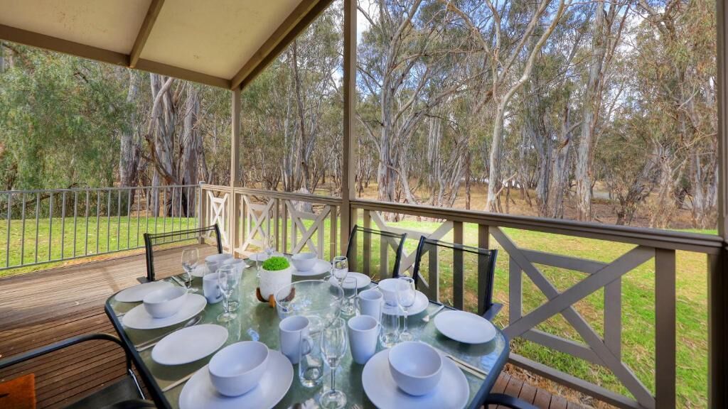 A covered outdoor dining area with a table set for a meal, surrounded by trees.