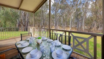 A covered outdoor dining area with a table set for a meal, surrounded by trees.