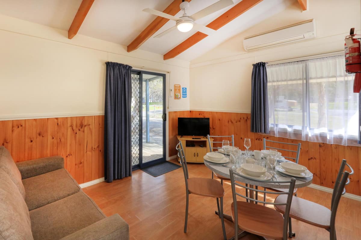 Una habitación amoblada con sofá, mesa de comedor, sillas, televisor y puerta corrediza de vidrio que da al exterior.