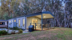 A modern, single-story house with a covered patio, a barbecue grill, and a trash can. - Deniliquin Riverside Caravan Park (Deniliquin)