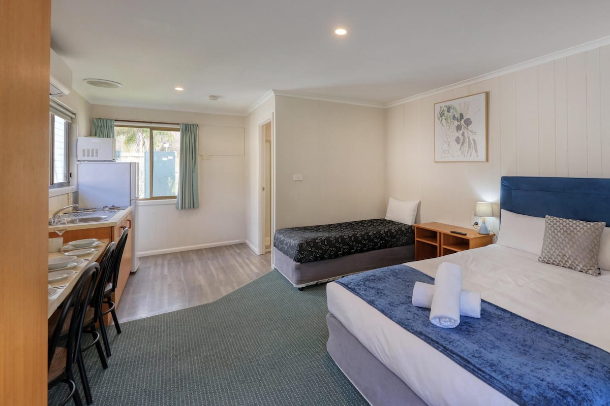 Una habitación de hotel con cama, una cama adicional, un escritorio con silla, una ventana y una puerta.
