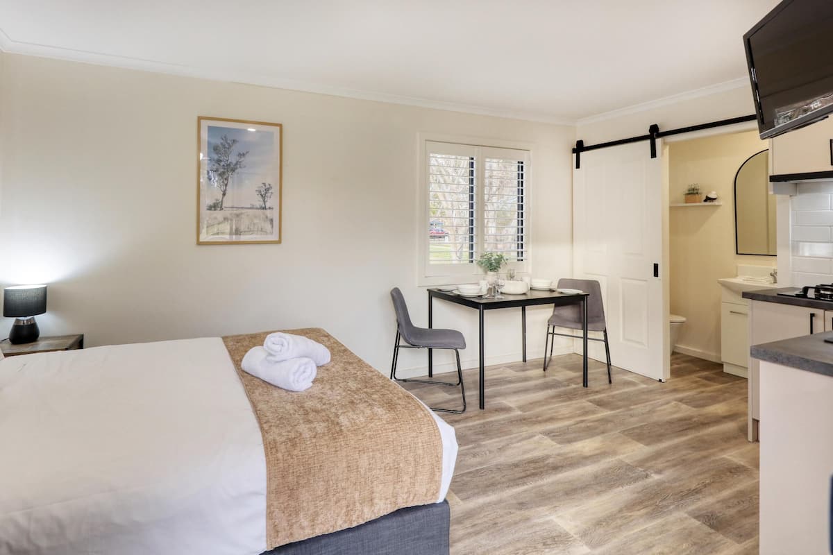 Una habitación de hotel con cama, escritorio, silla, una pequeña cocina y ventana.