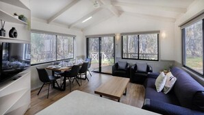 A spacious living area with a dining table, sofa, and large windows offering views of the outdoors. - Deniliquin Riverside Caravan Park (Deniliquin)