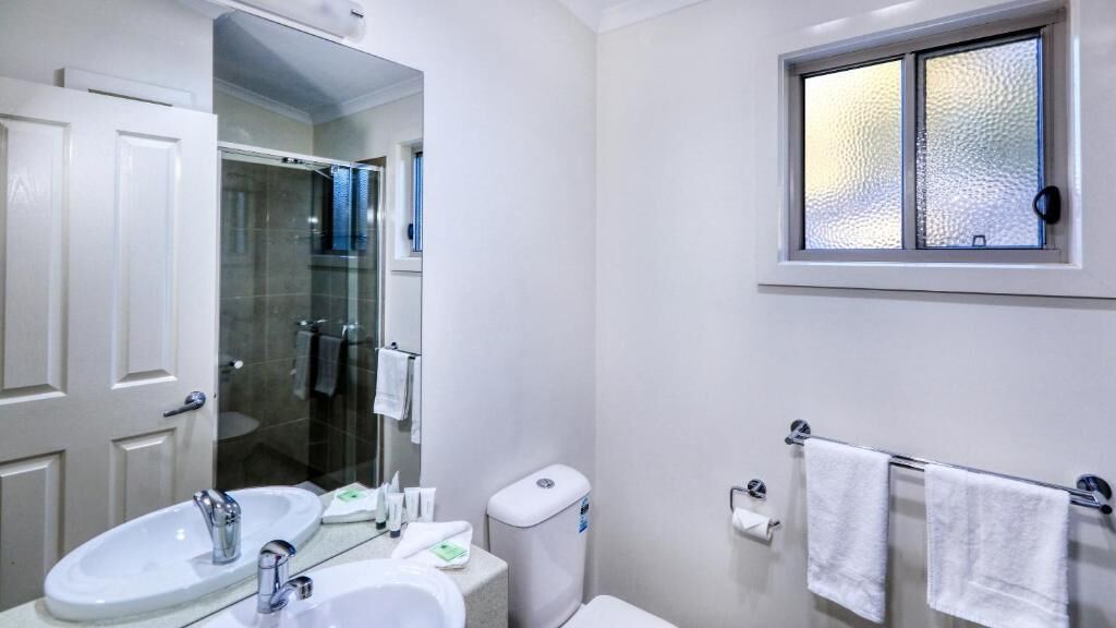 A bathroom with a sink, mirror, toilet, and towel rack.