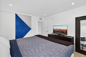 Ein modernes Schlafzimmer mit einem Bett, einem Fernseher und einem großen Spiegel.