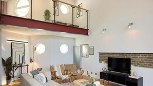 En moderne stue med sofa, sofabord og tv. Der er en balkon med gelændere og pejs.
