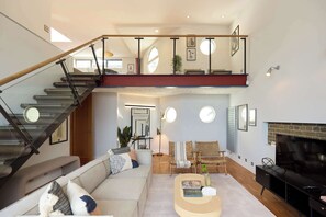A spacious living area with a staircase, a sofa, a coffee table, and a TV. - The Union Gallery Loft (London)