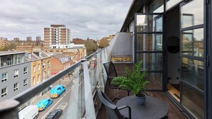 En balkon med udsigt til en gade, et bord med stole og en potteplante.