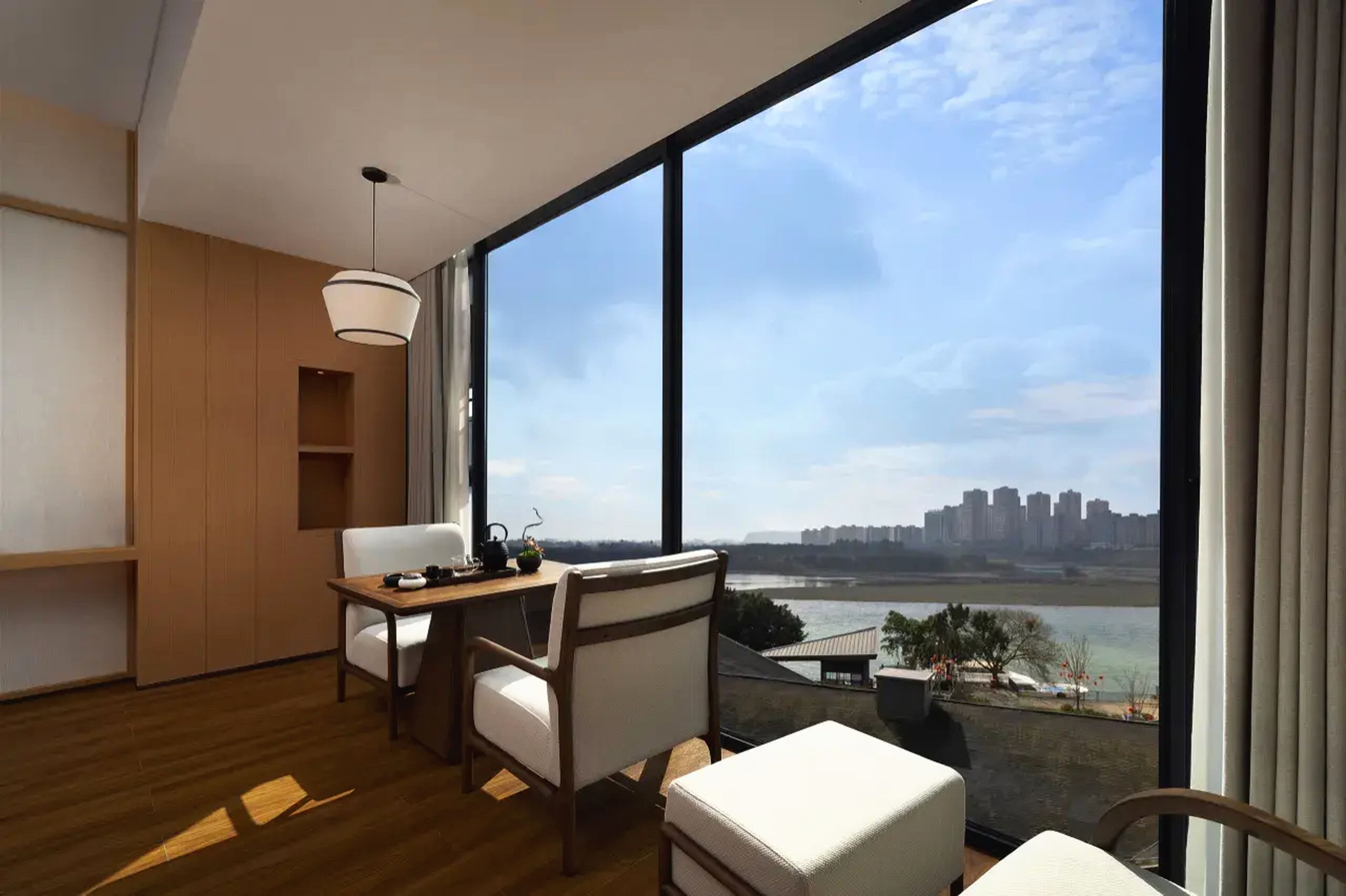 A modern room with a large window, a desk, two chairs, and a view of a river and city skyline.