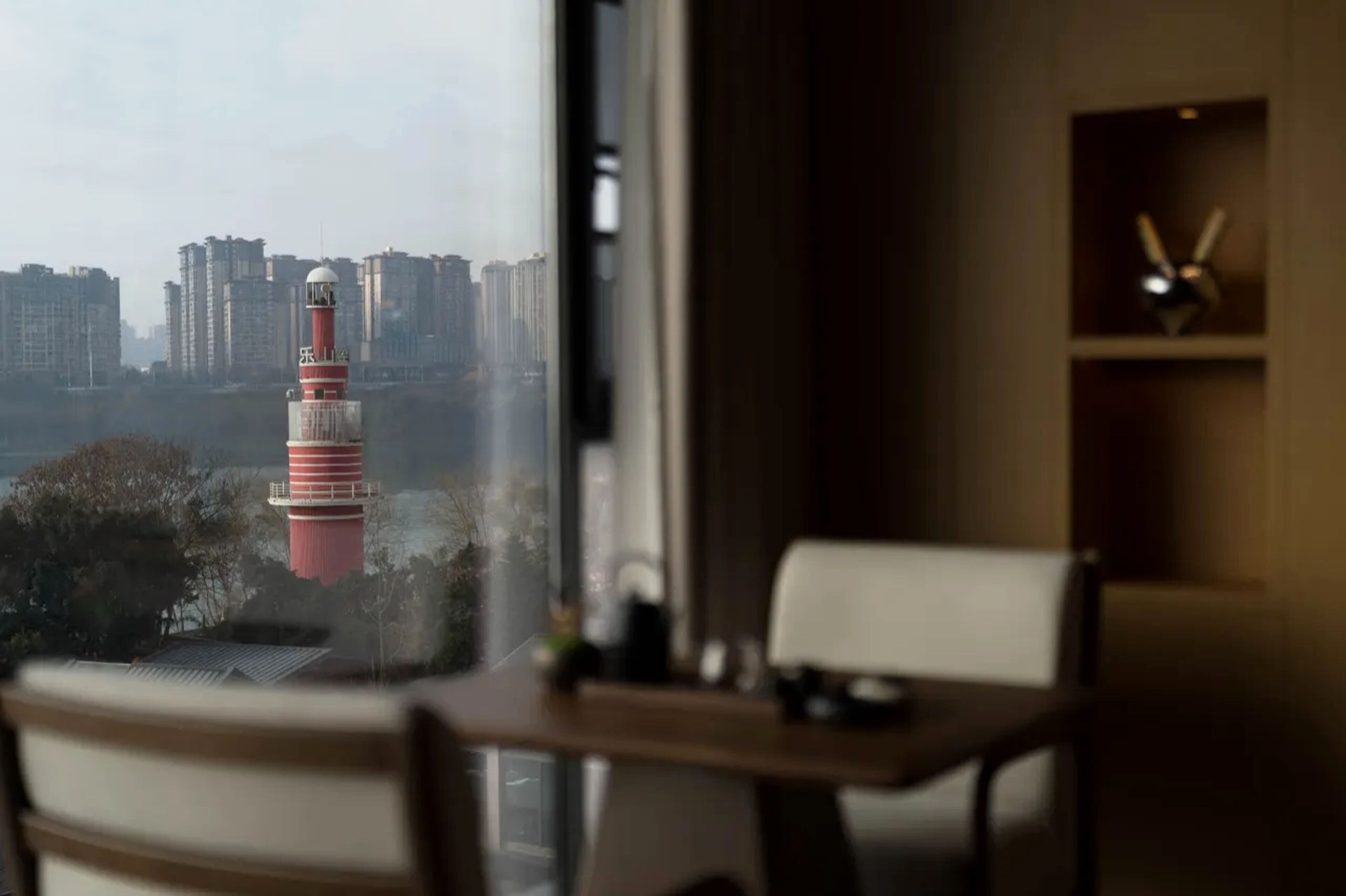 A room with a view of a tall building with a red and white tower, a wooden desk, and a chair.
