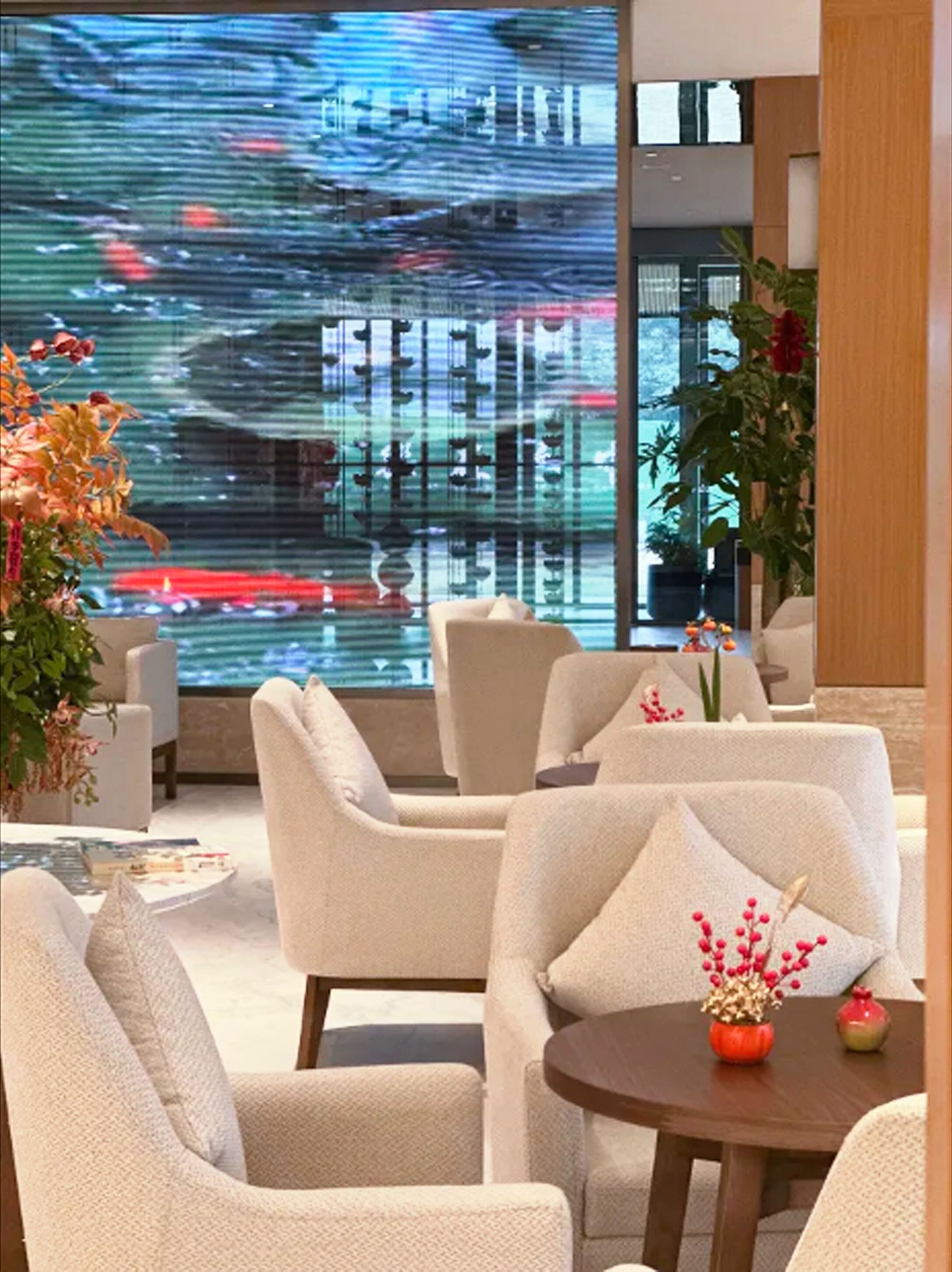 Un vestíbul d'hotel modern amb una gran pantalla digital que mostra un paisatge urbà, seients còmodes i plantes d'interior.