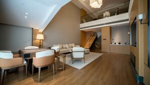 Una sala de estar moderna con un sofá, sillas, una mesa de centro y una mesa de comedor. Una escalera conduce a un nivel superior con un balcón.