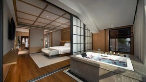 Habitación de hotel moderna con una cama grande, un vestidor amplio, una zona de estar y una bañera con pétalos de rosa.