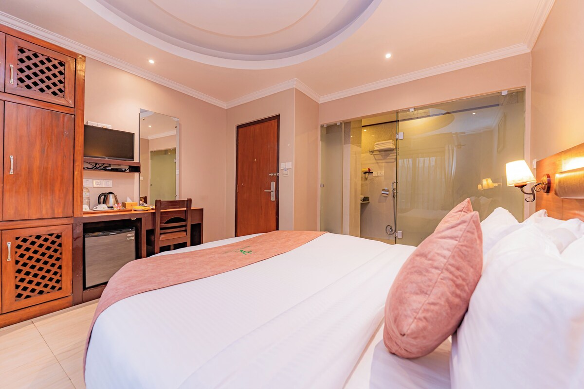 A hotel room with a bed, a desk, a mirror, a wardrobe, and a shower area.