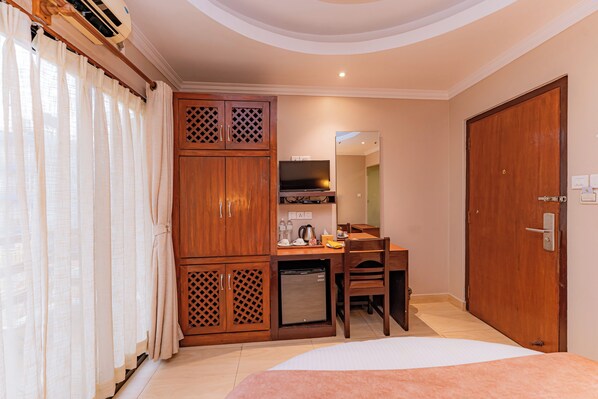 Une chambre d’hôtel comprenant un lit, un bureau avec une chaise, une télévision, un réfrigérateur et une armoire.