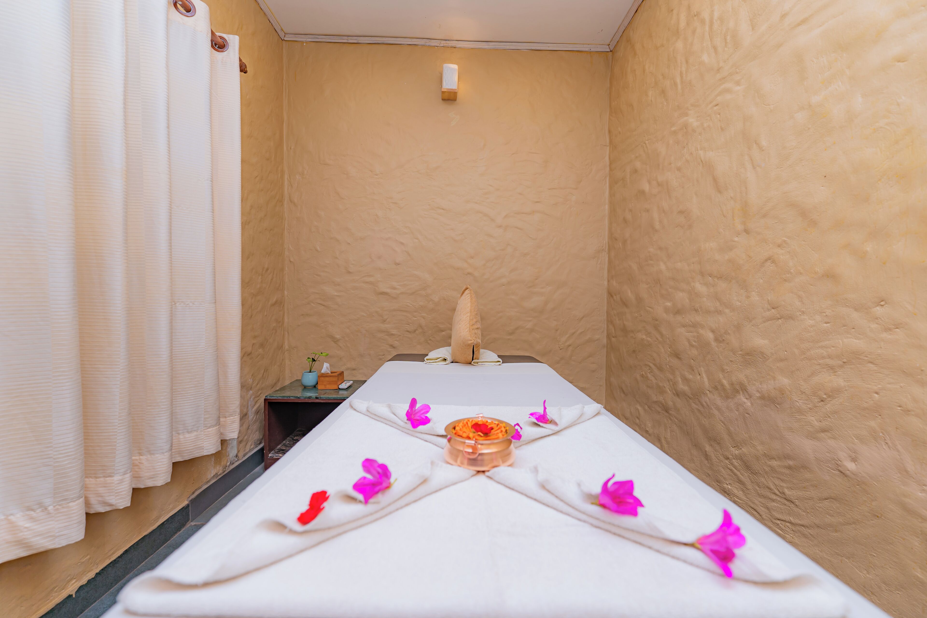 Um espaço de spa com uma mesa de massagem, um porta-toalhas e uma pequena mesa com uma vela.
