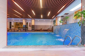 Une piscine intérieure avec un mur carrelé, des chaises longues et un plafond en bois.
