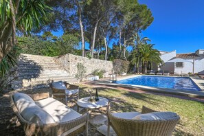 A poolside area with wicker furniture, a stone wall, and a clear blue sky. - Las Buganvillas - Javea, Costa Blanca (Javea)
