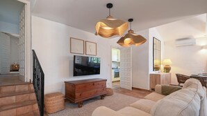 Ein Wohnzimmer mit Sofa, Fernseher, Holzkommode und einer Treppe.