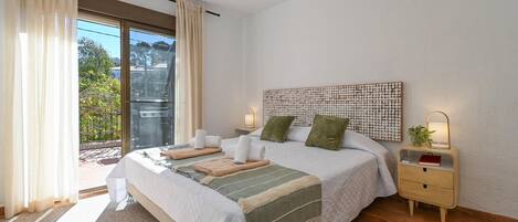 A bedroom with a bed, nightstands, a wall-mounted artwork, and a view through a sliding door.