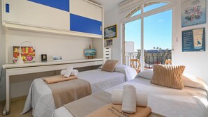 Ein Hotelzimmer mit zwei Betten, einem Schreibtisch, einem Fenster mit Balkonblick und Bildern an der Wand.