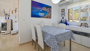 Eine moderne Küche mit Essbereich, einem Gemälde einer Küstenlandschaft und Blick durch das Fenster.