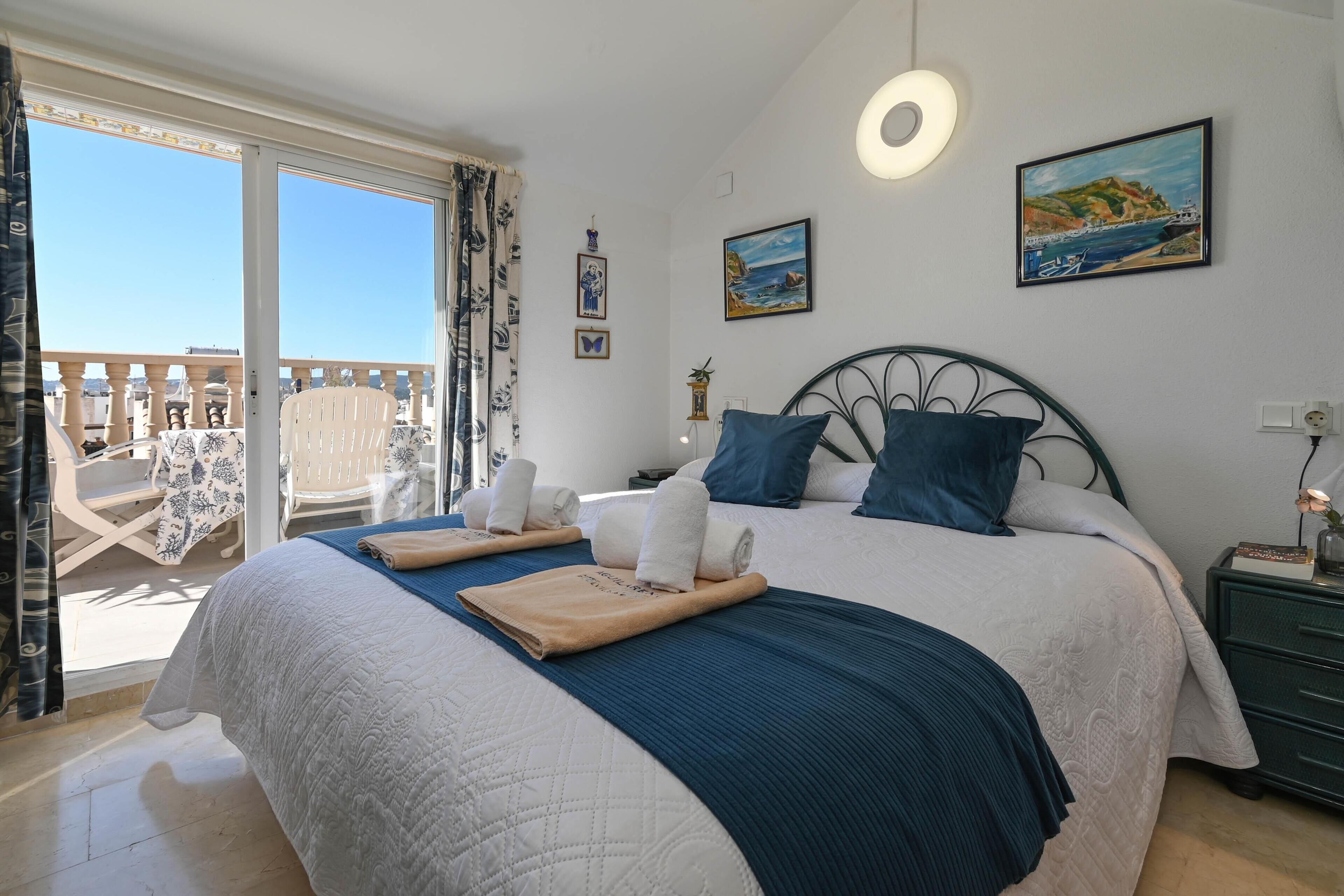 A bedroom with a bed, a nightstand, a window with a view, and a chair.