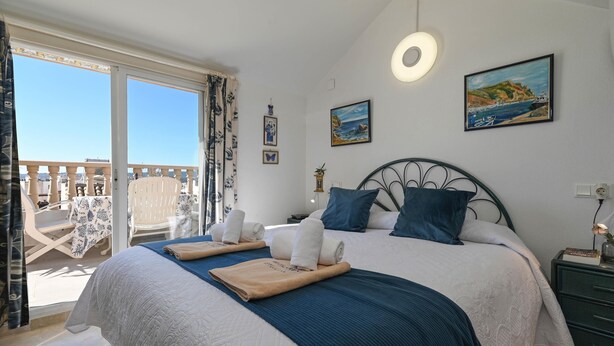 Ein Schlafzimmer mit Bett, Nachttisch, Fenster mit Blick und einem Sessel.