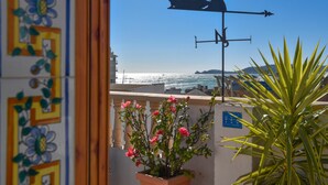 Ein Balkon mit Blumentopf, Wetterhahn und Blick auf das Meer.