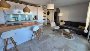 Una cocina moderna con una isla central, taburetes de bar, una mesa de comedor y un sofá en la sala.