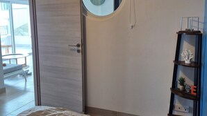 Un dormitorio con una cama, un espejo redondo, una puerta de madera y una estantería con objetos decorativos.