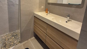 Un baño moderno con ducha, un espejo grande y un tocador con lavabo.