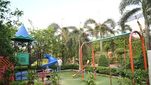 A playground with slides, swings, and climbing structures surrounded by potted plants and palm trees. - Sanzha Chulha Hotel (Varanasi)