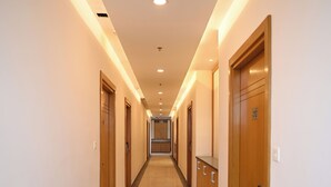 A long, well-lit hallway with wooden doors and a marble floor. - Sanzha Chulha Hotel (Varanasi)
