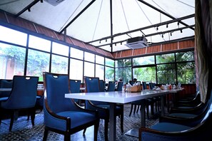 Un restaurante con una mesa larga, sillas azules y ventanas amplias.