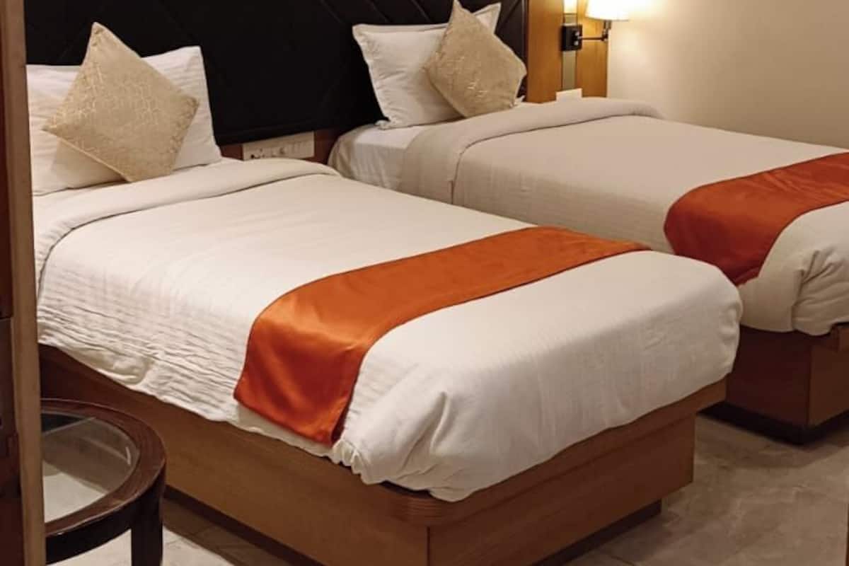 Habitación de hotel con dos camas, cabecero de madera, mesita de noche y ventilador de techo.