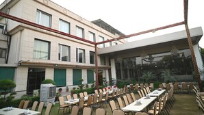 A hotel with outdoor dining area, multiple tables and chairs, and a large building with windows and a covered section. - Sanzha Chulha Hotel (Varanasi)
