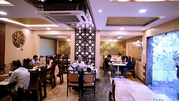 A restaurant with multiple dining tables, chairs, and a decorative wall with a floral pattern. - Sanzha Chulha Hotel (Varanasi)