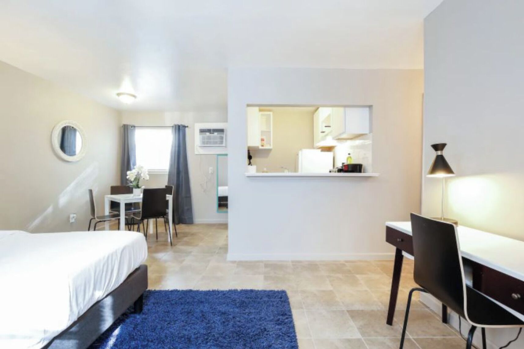 A compact hotel room with a bed, desk, chair, and kitchenette.