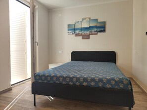 A bedroom with a bed, a nightstand, a wall-mounted artwork, and a sliding glass door. - Holiday Home Casa Simone in Lido (Camaiore)