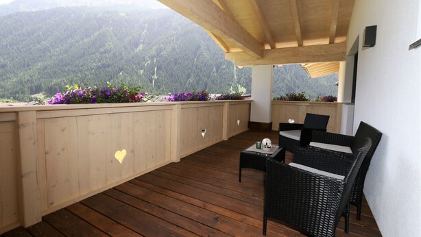 A wooden deck with wicker furniture, a heart-shaped cutout on the wall, and a mountainous backdrop. - Apartment in Milders With Stubai Supercard (Neustift Im Stubaital)