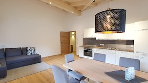 A modern kitchen with a wooden table and chairs, a sofa, and a pendant light. - Apartment in Milders With Stubai Supercard (Neustift Im Stubaital)