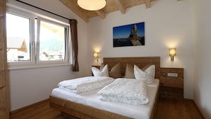 A wooden-framed bedroom with a bed, two bedside lamps, and a mountain view through the window. - Apartment in Milders With Stubai Supercard (Neustift Im Stubaital)